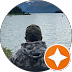 Person in camo jacket and hat facing water with mountains in the background