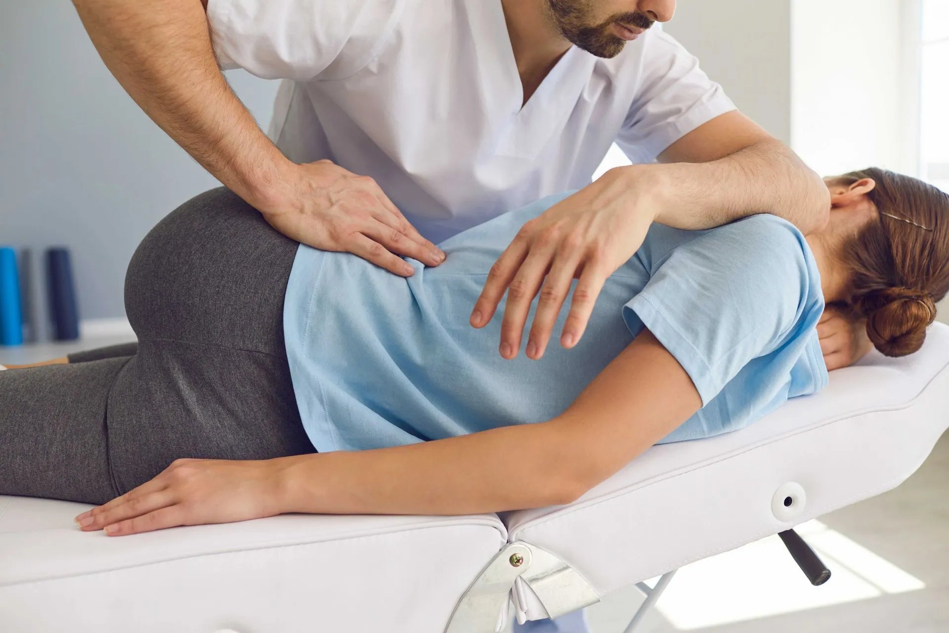 Chiropractor adjusting a woman lying face down on a treatment table in a clinic.