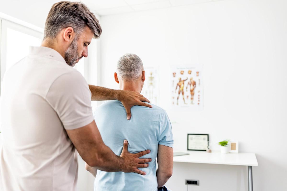 Therapist performing back therapy on a seated man wearing a light blue shirt in a bright office.
