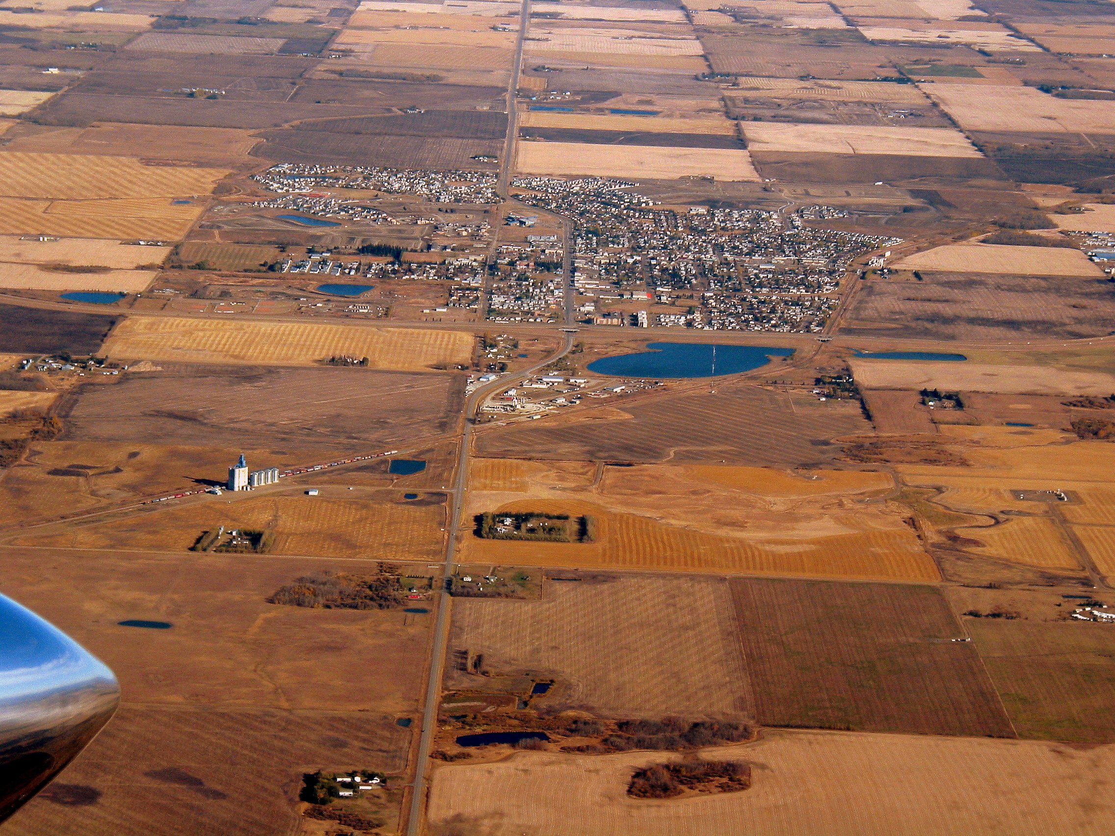 Aerial view of farmland, roads, and a small town with ponds and buildings in a rural area.