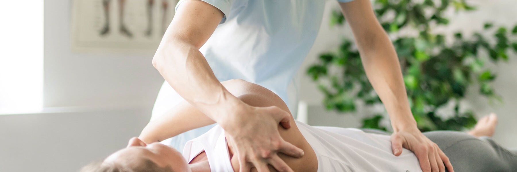 Therapist in light blue shirt performing shoulder stretch on a woman lying down wearing white top