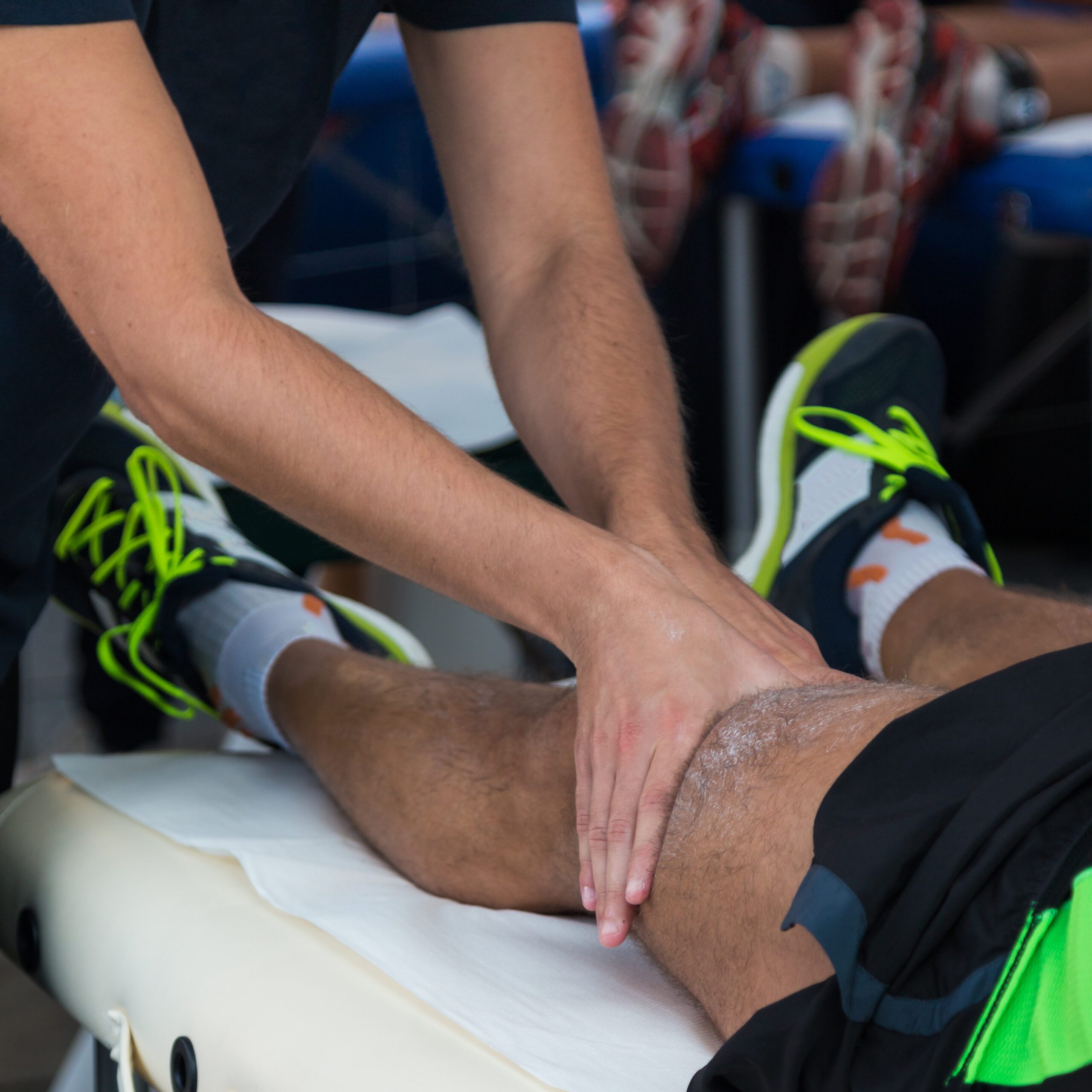 Therapist massaging a male athlete's leg on a treatment table wearing neon-accented running shoes.