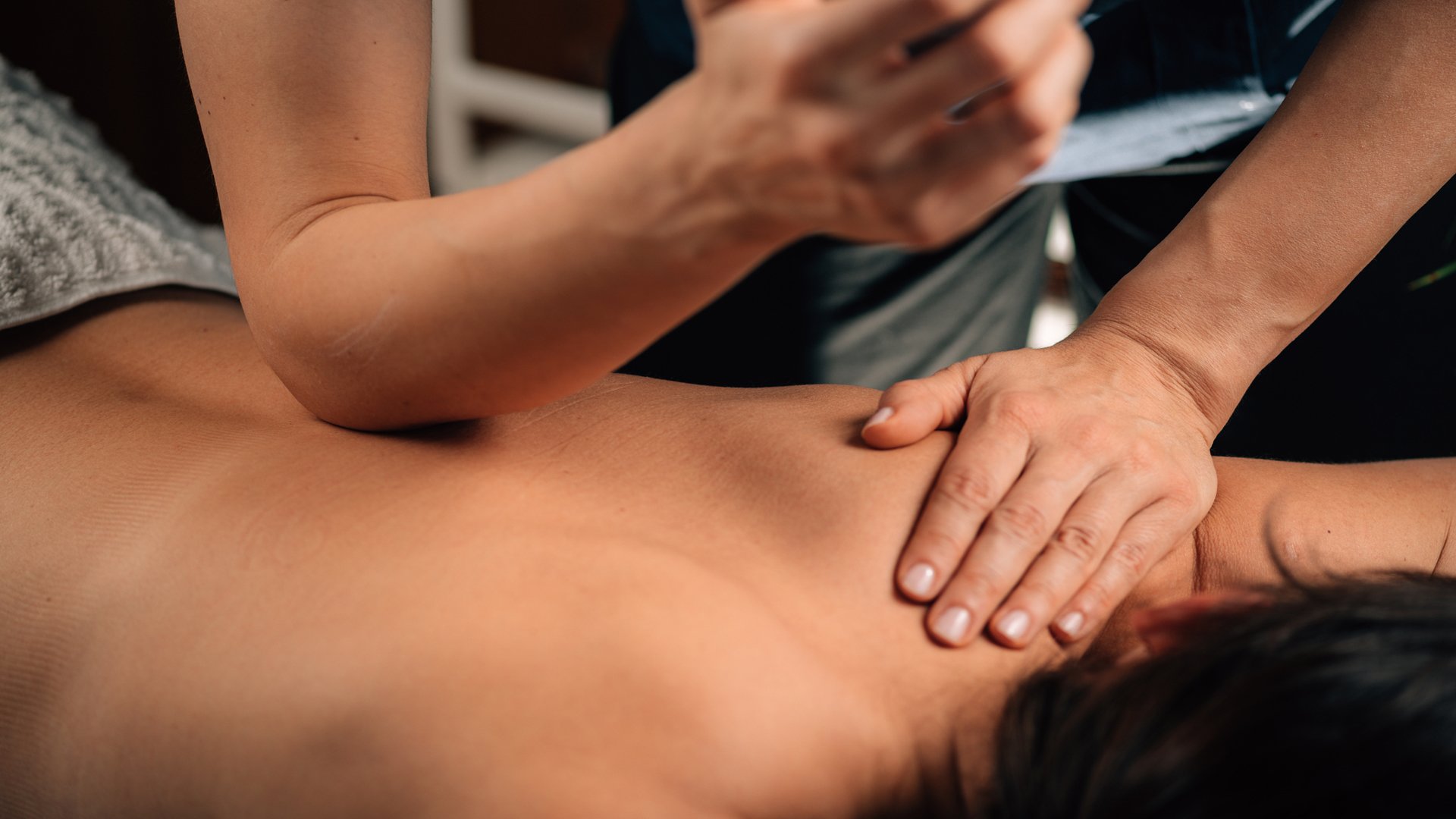 Close-up of a person receiving a shoulder and upper back massage from a therapist.