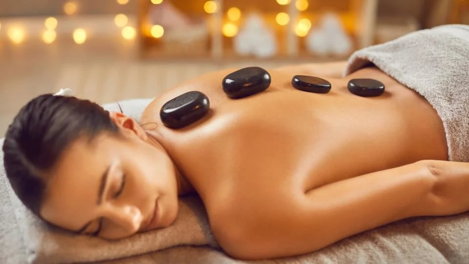 Woman lying face down with hot stones on her back in a softly lit spa setting.