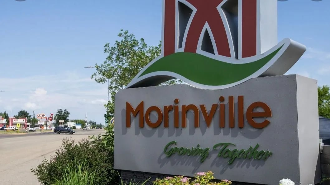 Morinville sign with 'Growing Together' slogan beside a street with trees and businesses like KFC and A&W.