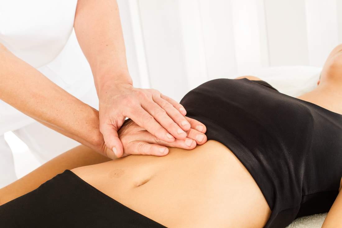 Therapist performing abdominal massage on a person lying down wearing a black top.