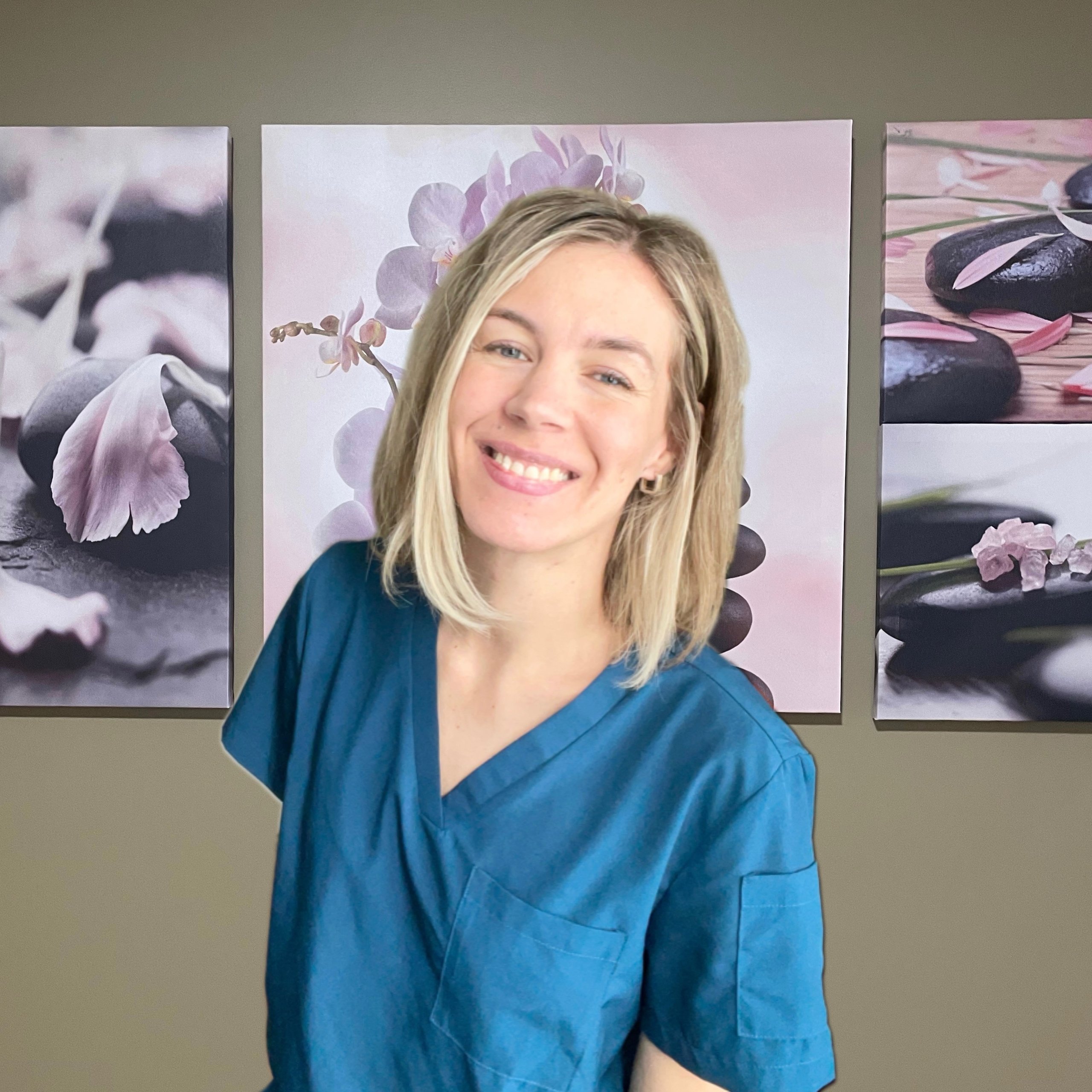 Smiling woman in blue scrubs stands before wall art featuring pink flowers and black stones.
